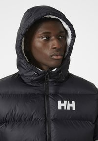 Chaqueta acolchada negra con capucha, que presenta un logo blanco en el pecho, un acabado texturizado y un cierre de cremallera. Forrada con un interior de contraste.