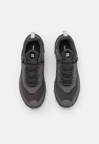 Zapatillas deportivas negras con parte superior de malla texturizada, punta redonda, diseño de cordones y un collar y suela acolchados, con una suela exterior gris.