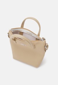 Borsa a mano in sintetico beige con esterno testurizzato, doppio manico, chiusura con zip e branding interno. Dotata di parti in metallo e design minimalista.