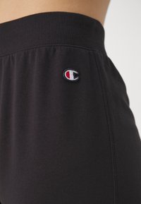 Black sweatpants made of soft fabric with a ribbed waistband. Features a small white and red embroidered logo on the side.