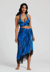Blå halterneck crop top med en knytkjol som har abstrakta mönster och svarta fransar längs fållen. Slät tygtextur.