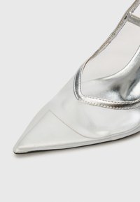 Sølv stiletto hæl sko med spiss tå, som har en glatt satengfinish, gjennomsiktige sidepanelet og et strømlinjeformet design.
