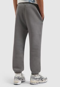 Grijze sweatpants met een ontspannen pasvorm, elastische boorden en zijzakken. Gecombineerd met lichtgrijze sportschoenen met zilveren accenten.