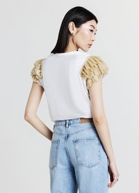 Top bianco a maniche corte con dettagli in rouches beige testurizzate sulle spalle, abbinato a jeans a vita alta e lavaggio chiaro. Vista posteriore.