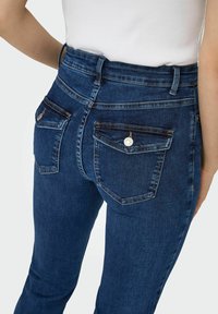 Niebieskie dżinsy z wysokim stanem i dopasowanym krojem, z dwoma tylnymi kieszeniami z srebrnymi guzikami oraz delikatnym przecieraniem wzdłuż szwów.