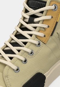 Ανοιχτό πράσινο αθλητικό παπούτσι με λευκά κορδόνια, μαύρες λεπτομέρειες και υφασμένο ελαστικό πάτο. Διαθέτει κίτρινη και μαύρη ετικέτα κοντά στα κορδόνια.