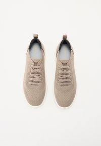 Beige hálós tornacipő texturált felülettel, kerek orral és fehér talppal. Zsinórokkal és húzópánttal a saroknál a könnyű felvétel érdekében.