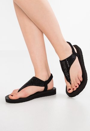 Czarne sandały na cienkiej podeszwie typu thong z fakturowaną cholewką ozdobioną brokatem, miękką gumową podeszwą i cienkim paskiem wokół kostki.