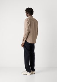 Vaaleanruskea pitkähihaisessa paidassa on napit, ja se on yhdistetty tummansinisiin housuihin. Kengissä on beige ja harmaa värisävy yhdistelmä.