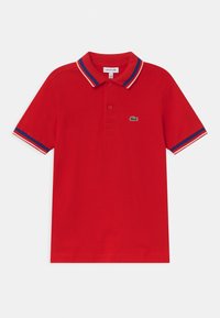 Červené polo tričko s krátkým rukávem, se modrým, bílým a červeným lemem na límci a rukávech, na hrudi má malé zelené logo krokodýla.