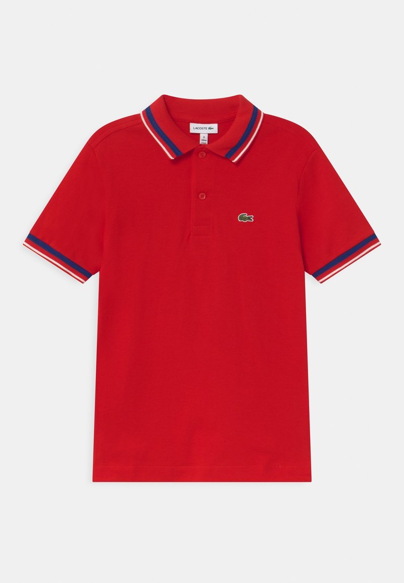 Červené polo tričko s krátkým rukávem, se modrým, bílým a červeným lemem na límci a rukávech, na hrudi má malé zelené logo krokodýla.