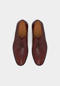 Ζευγάρι γυαλισμένα καφέ δερμάτινα παπούτσια δεμένα με κορδόνια, σε θέα από πάνω πάνω σε ουδέτερο φόντο.