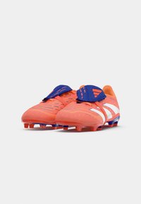 Botas de fútbol de color naranja brillante con rayas blancas, material texturizado, acentos azules en el talón y correas de Velcro para un ajuste seguro.