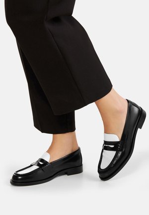 Czarne mokasyny ze skóry z białym skórzanym akcentem i ozdobnym czarnym paskiem, z niskim obcasem i gładką teksturą.
