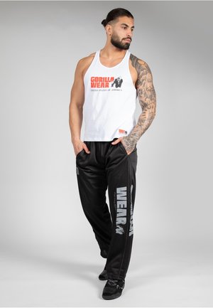 White tank top with red and black "GORILLA WEAR" logo, paired with black sweatpants featuring gray branding. Smooth fabric, athletic fit.
