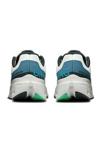 Baskets de sport blanches avec des accents vert foncé et bleu, un talon texturé et un motif de semelle visible avec des détails de marque.