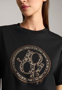 Zwarte katoen t-shirt met een cirkelvormige luipaardprint en metallic accenten in het logo. Ronde hals en korte mouwen compleet maken het ontwerp.