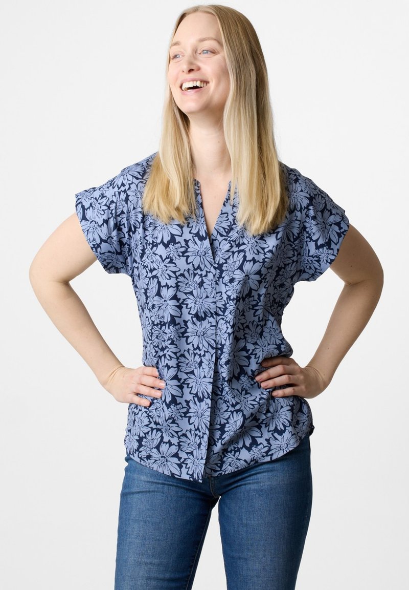 Blusa corta a maniche corte con stampa floreale blu e chiusura a bottoni, realizzata in un tessuto leggero e con una vestibilità ampia, abbinata a jeans blu.