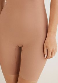 Shorts gainants taille haute en tissu lisse de couleur brun clair, d'une longueur mi-cuisse avec une petite ouverture à l'entrejambe.