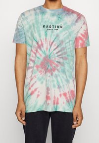 Koszulka z krótkim rękawem w efekt tie-dye w pastelowych odcieniach niebieskiego, zieleni i różu, z wzorem w spiralę. Na piersi znajduje się czarny napis "KAOTIKO".