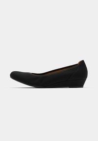 Scarpa piatta nera con punta arrotondata, tomaia in tessuto morbido e tacco a zeppa basso. Caratterizzata da un design semplice e lineare e hardware minimale.