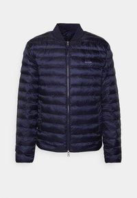 Giacca puffer blu navy con zip frontale, colletto a coste, motivo a righe orizzontali e un logo discreto sul petto. Materiale liscio e leggero.