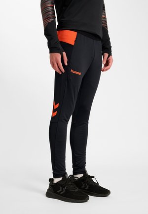 Pantaloni sportivi neri con accenti arancioni e motivi a chevron. Realizzati in tessuto liscio con un design aderente per comfort e flessibilità.