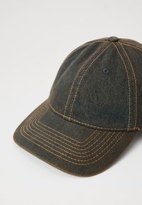 Denim baseball kapa v temno modri barvi z kontrastnim oranžnim šivom. Ima ukrivljen rob in zračnike. Mehak material.