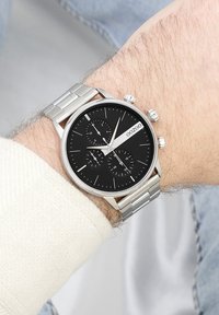 Montre en acier inoxydable argenté avec un cadran noir, des accents argentés, trois sous-cadrans et un bracelet lisse et poli.