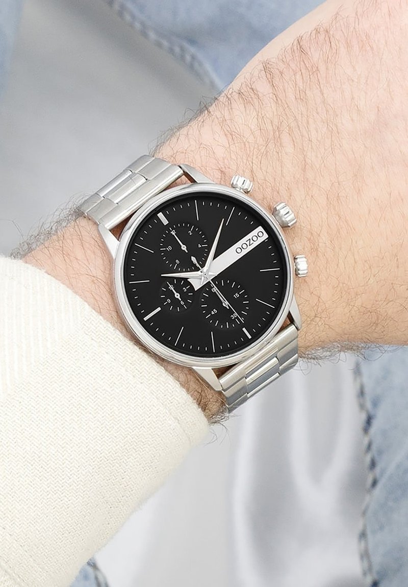 Montre en acier inoxydable argenté avec un cadran noir, des accents argentés, trois sous-cadrans et un bracelet lisse et poli.