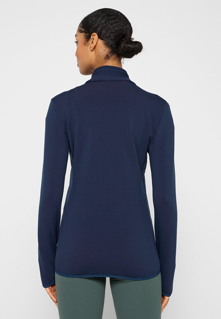 Haut à manches longues bleu marine avec un tissu texturé, col haut et coupe ajustée, présentant un ourlet arrondi et une finition contrastante à la base.