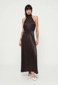 Vestido maxi de cetim preto com decote halter, corpete ajustado, saia fluida e textura suave. Apresenta gola alta e brilho subtil.