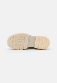 Suela de calzado de goma suave en color crema, con un diseño de banda de rodadura estampada. Presenta un logotipo en relieve y un diseño de punta redondeada.
