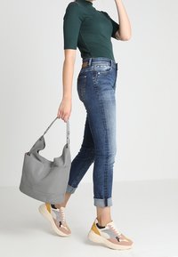 Vihreä lyhythihainen paita, siniset kapenevat farkut, vaaleanharmaa olkalaukku ja moniväriset paksupohjaiset lenkkitossut, joissa on vaaleanpunaisia, keltaisia ja harmaita yksityiskohtia.