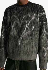 Puhafekete és szürke pulóver lekerekített nyakkivágással, textúrált mintával és bordás mandzsettával, valamint aljjal. Sötét nadrág felett viselve.