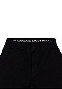 Pantalon baggy noir avec poches avant et fermeture à bouton, avec le texte "THE ORIGINAL BAGGY PANTS" sur la ceinture intérieure.