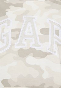 Felpa beige a motivo mimetico con grande scritta "GAP" ricamata in bianco e con cuciture in rilievo sul davanti. Tessuto morbido e casual.