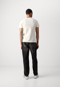Lysfarvet kortærmet t-shirt med rund hals, parret med sorte denimbukser med lige pasform og synlige syningsdetaljer.