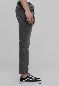 Jeans gris de corte slim con cinco bolsillos, un sutil desgaste y pierna ligeramente ajustada, combinados con zapatillas Vans negras.
