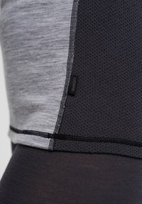 Grå atletisk top med et sort mesh sidepanel, der har kontraststing og et lille mærke. Glat tekstur med en tætsiddende design.