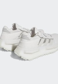 Adidași albi cu un superior texturat din tricot, accente argintii și o talpă groasă, translucidă, cu un model de tracțiune robust.