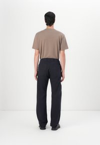 Bruin kortemmige t-shirt gecombineerd met marineblauwe cargobroek met zijzakken en een losse pasvorm, gezien vanaf de achterkant tegen een witte achtergrond.