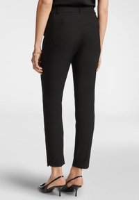 Pantaloni neri su misura con vestibilità slim, dotati di tasche posteriori e una leggera fessura alla caviglia. La texture del tessuto morbido completa il design.