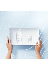 Biotherm hudplejesæt i hvide flasker placeret i en lyseblå kasse, der indeholder en stor pumpeflaske og en lille tube. Glatte, blanke overflader.