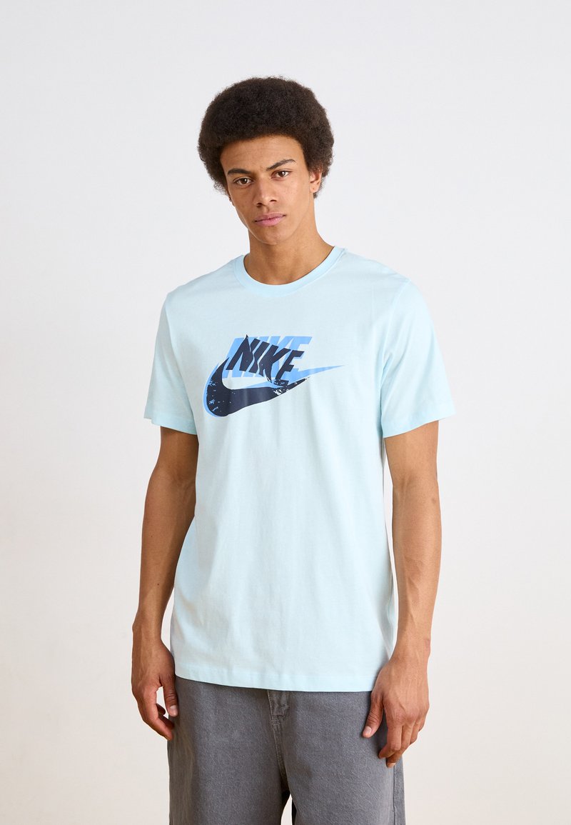Světle modré bavlněné tričko s tmavě modrým logem Nike a grafickým designem. Klasický výstřih, krátké rukávy, uvolněný střih.