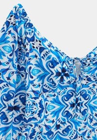 Tissu bleu et blanc à motifs floraux et géométriques, comportant des sections élastiques froncées et un petit détail à lacets.