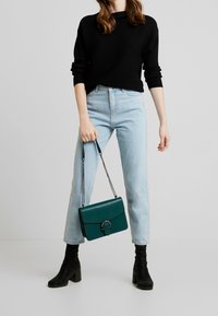 Černý žebrovaný svetr, světle modré džíny se širokými nohavicemi, černé boty na podpatku a petrolejová kabelka s detaily stříbrného řetízku a zapínání.