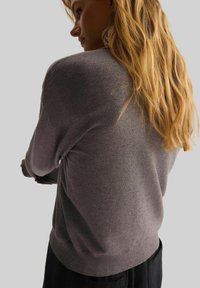 Szary, lekki sweter dzianinowy z okrągłym dekoltem i długimi rękawami. Subtelna tekstura, prążkowane mankiety i dół oraz luźny krój.