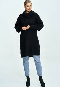 Czarny, oversize sweter z dzianiny z wysokim golfem, z prążkowanymi mankietami i luźnym krojem, w połączeniu z jasnoniebieskimi dżinsami i czarnymi botkami za kostkę.