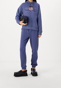 Felpa viola con logo, pantaloni jogger coordinati e scarpe platform nere. Tessuto morbido, vestibilità comoda e polsini elastici sui pantaloni.